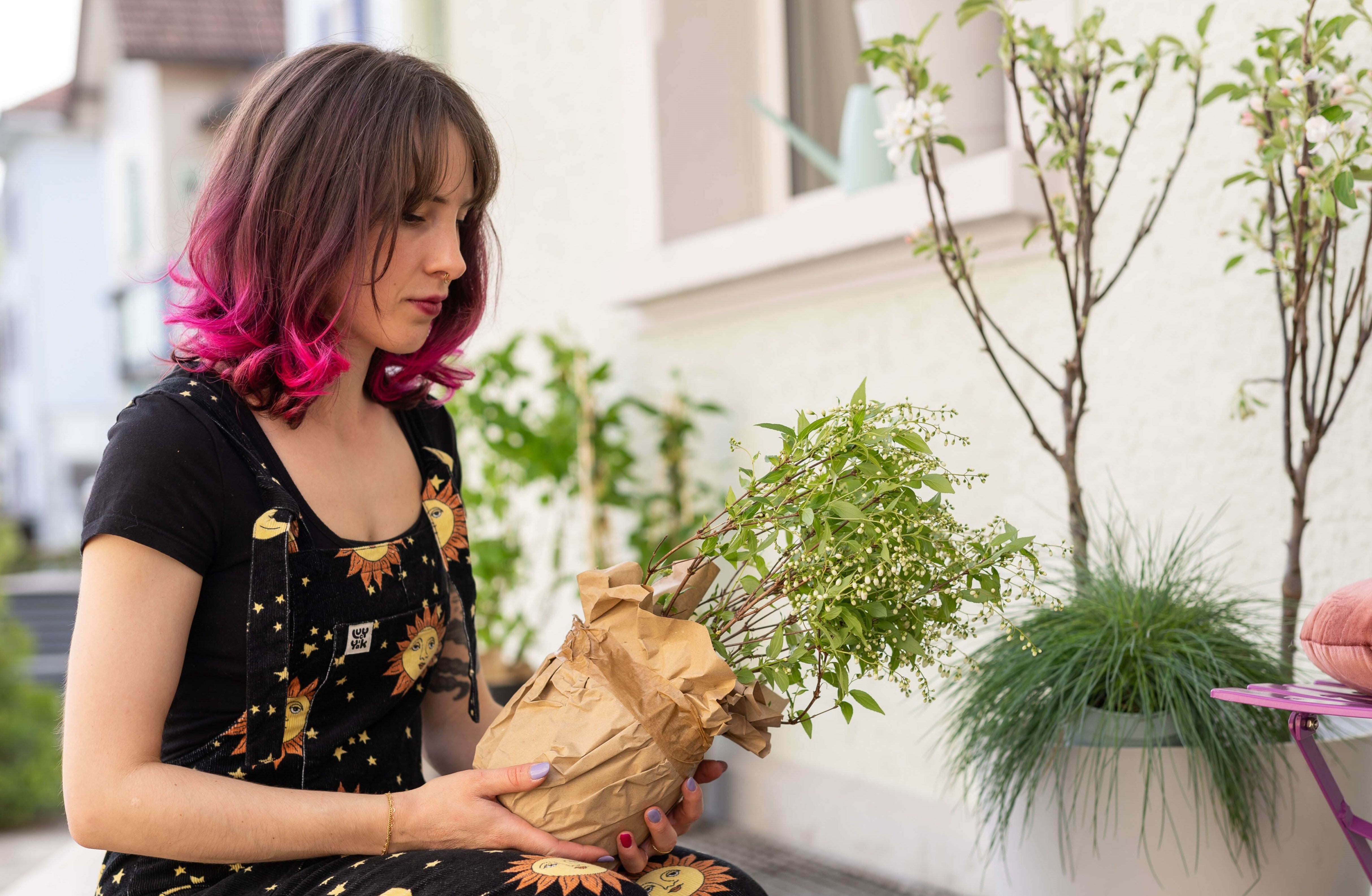 Frau mit pinken Haaren hält eine eingepackte Gartenpflanze in den Händen