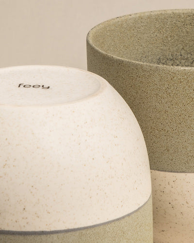 Nahaufnahme von zwei strukturierten, gesprenkelten Keramik-Pflanzgefäßen, eines beige und das andere graugrün. Im Vordergrund ist der Boden eines Keramik-Topfsets „Variado“ (22, 14, 2 × 7) mit dem Markennamen „Feey“ zu sehen. Beide Pflanzgefäße haben ein minimalistisches und natürliches Design, perfekt für Zimmerpflanzen.