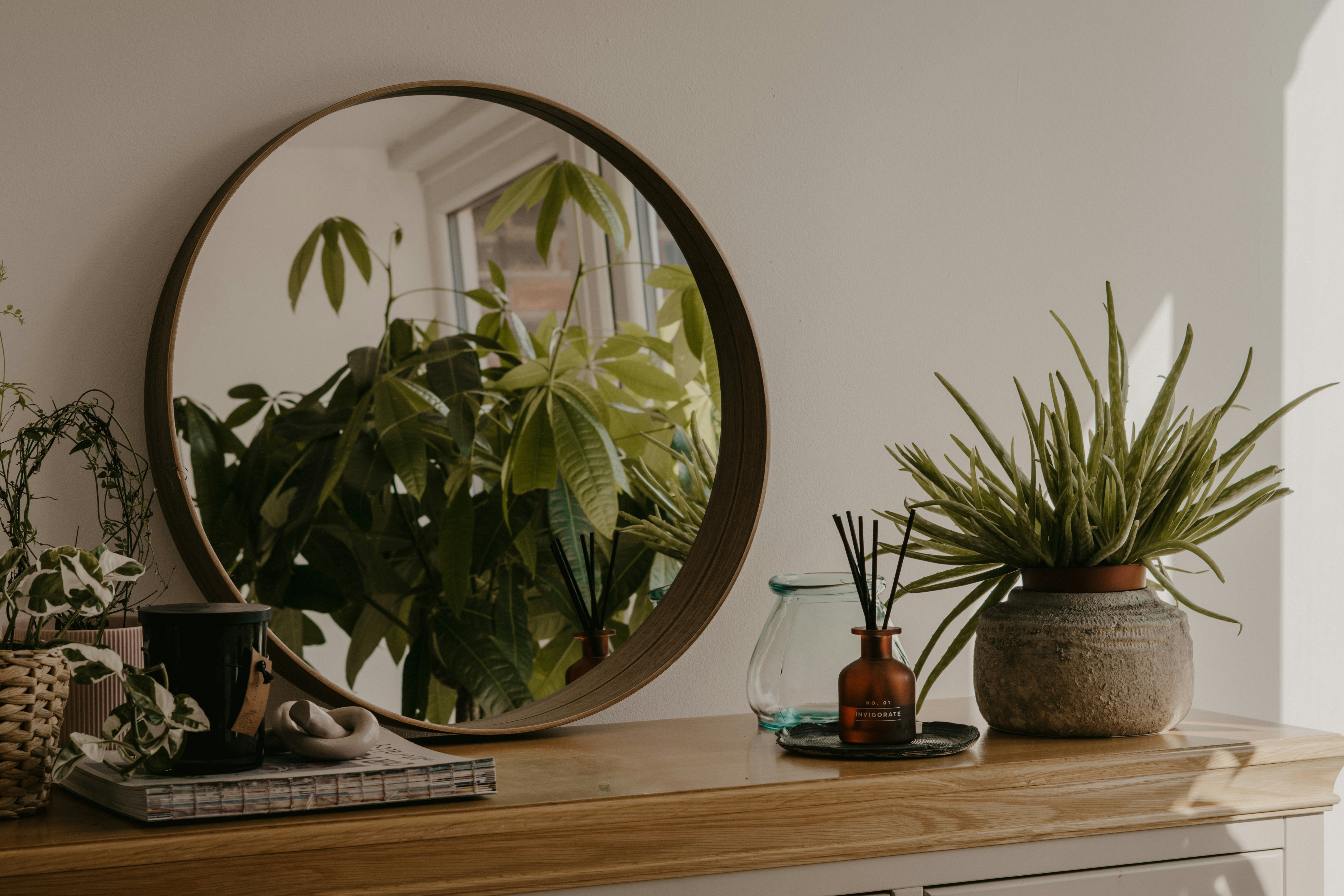 Ein Sideboard mit Pflanzen, Spiegel, Vase und Heft.