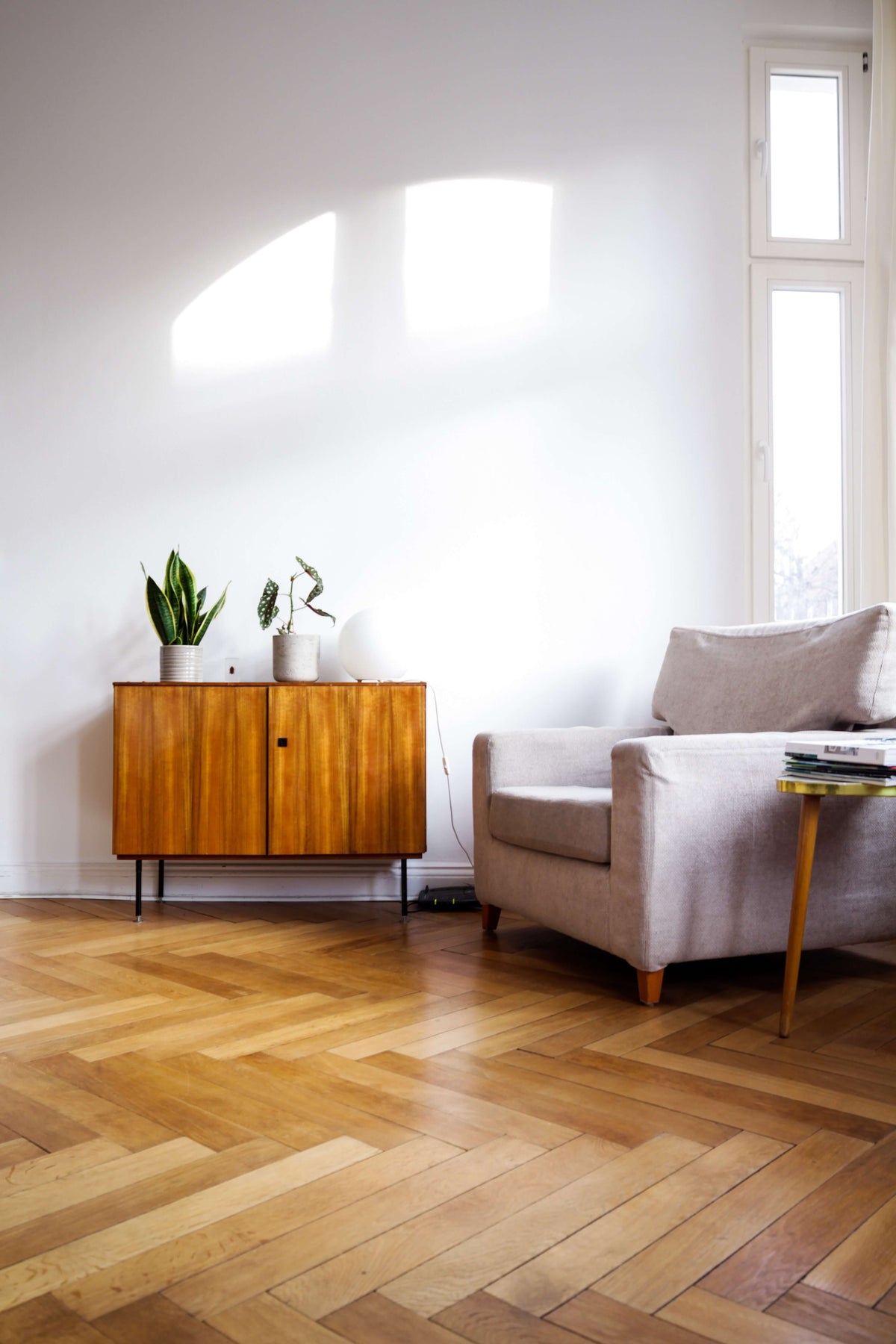 Sansevieria und Forellenbegonie auf einem schlichten hölzernen Sideboard, daneben ein weisser Sessel