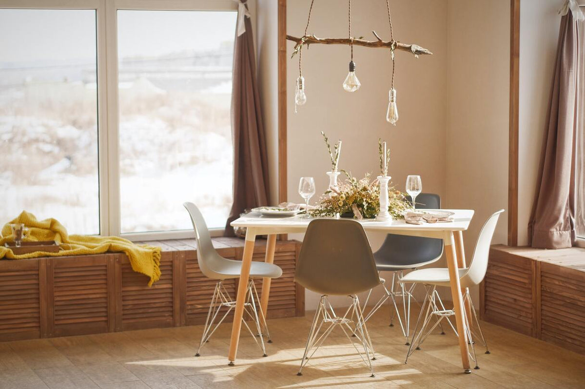 Weisser Tisch, schlichte Stühle, hölzerne Fensterbänke und Holzboden, ein Trockenblumen-Gesteck auf dem Tisch, darüber eine Lampe aus einem Stück Treibholz