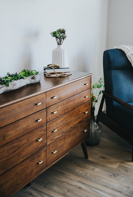 Kleine Pflanzen auf einem grossen, dunklen Sideboard, davor ein dunkler Sessel