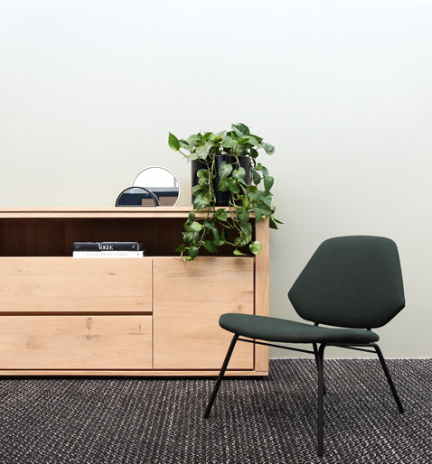 Hölzernes Sideboard mit einer buschigen Efeutute an einem Ende, davor ein Stuhl auf einem Teppich