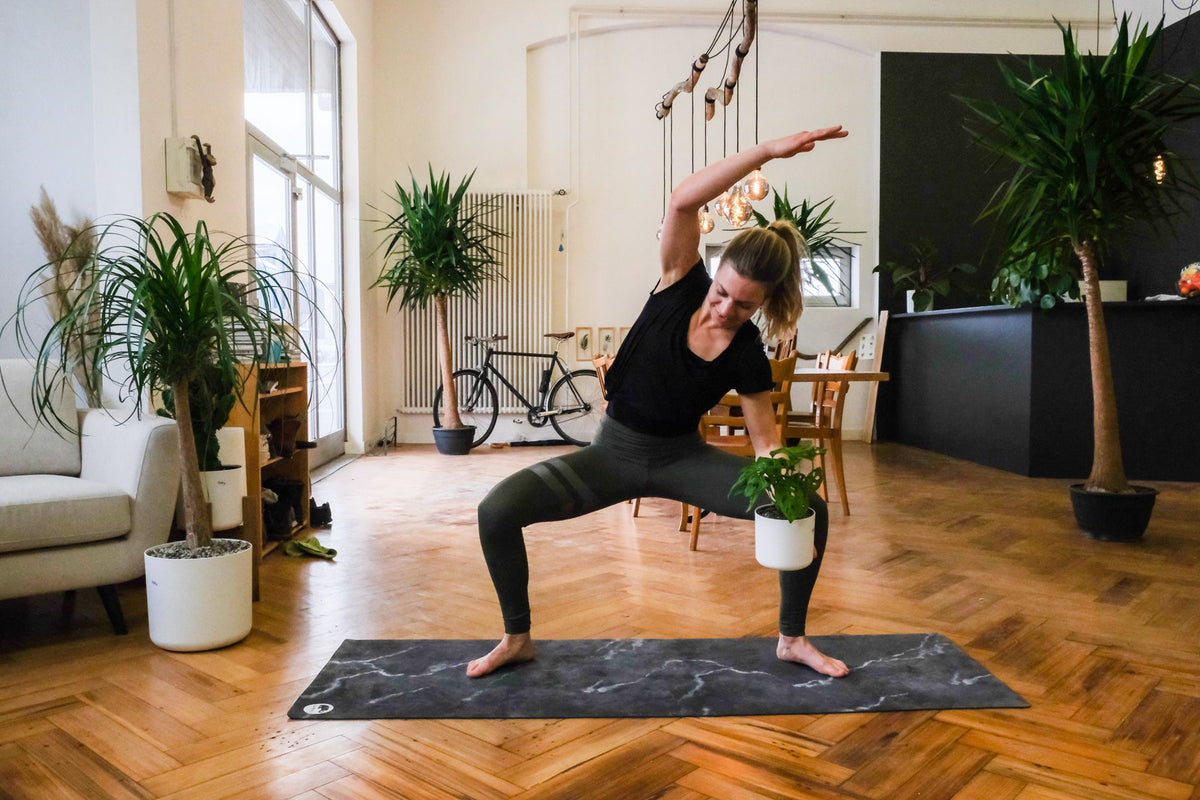 Plant-Yogi Hanna steht mit gebeugten Knien auf die linke Seite geneigt da, in der linken Hand, die auf dem linken Oberschenkel ruht, die feey-Pflanze