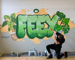 Sevi vor der besprayten Wand mit dem feey-Logo.